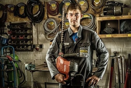 Tobias Kuennen der eine große Bohrmaschine in der Hand hält, in Arbeitskleidung